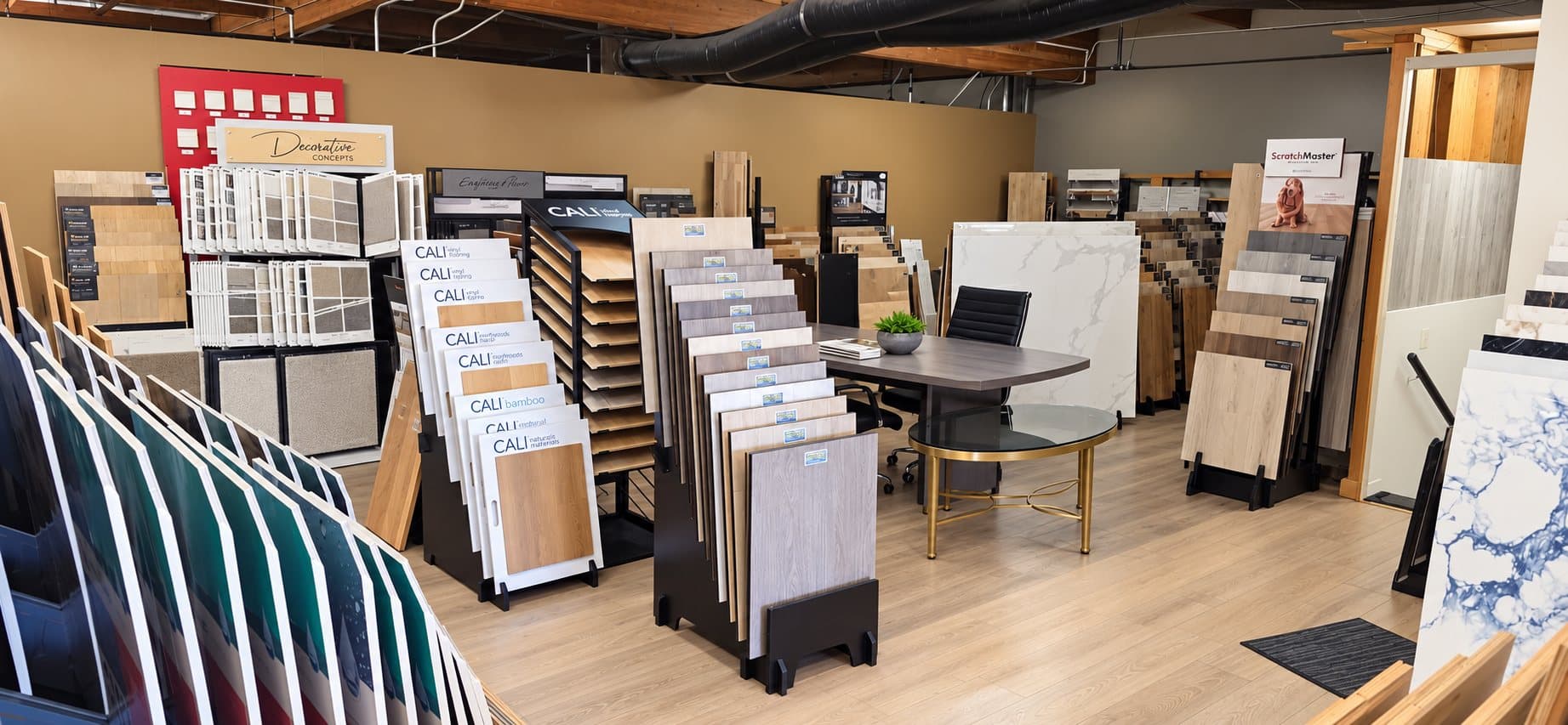 Selection table in the V & A Flooring Inc showroom surrounded by vinyl plank, laminate, carpet and tile sample displays