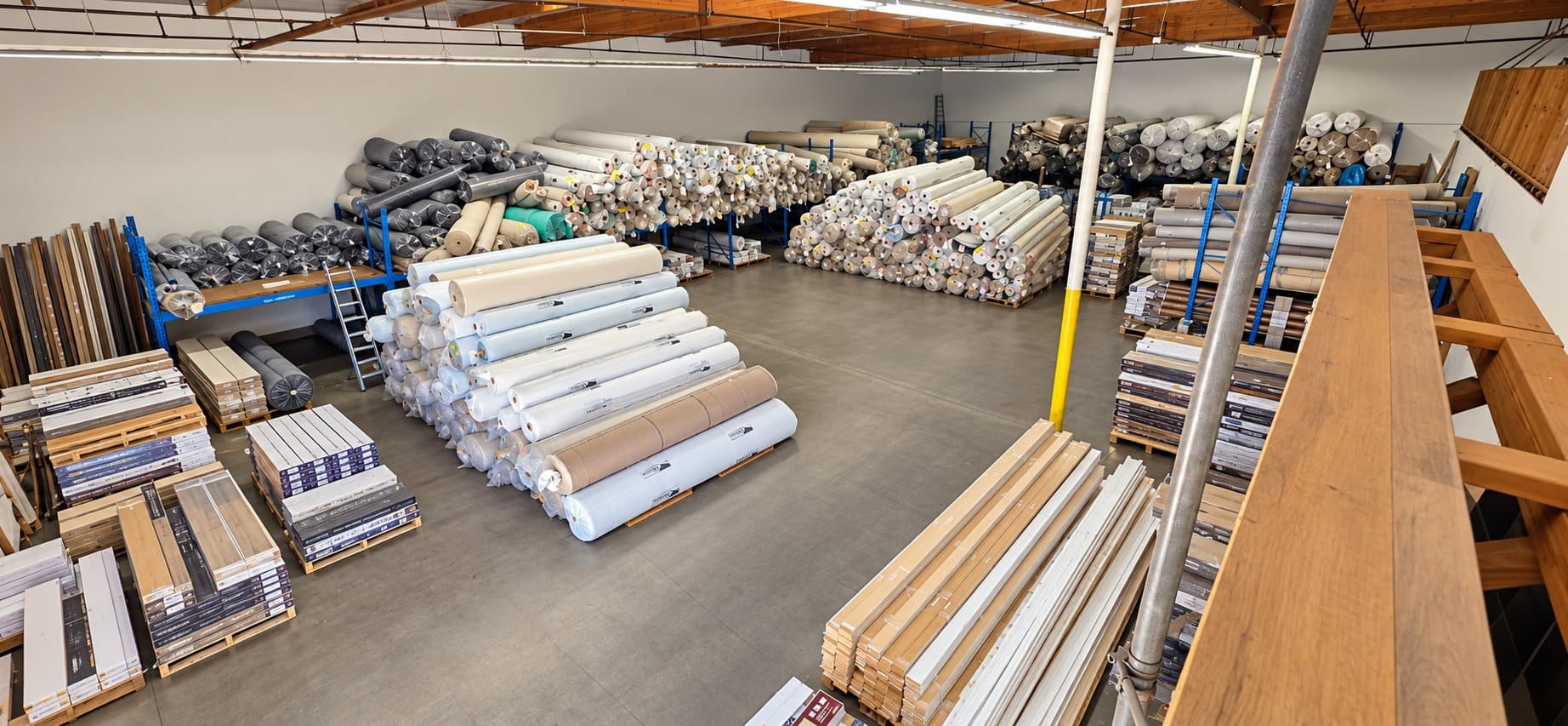 V & A Flooring Inc warehouse with carpet rolls, pallets of plank flooring and moldings
